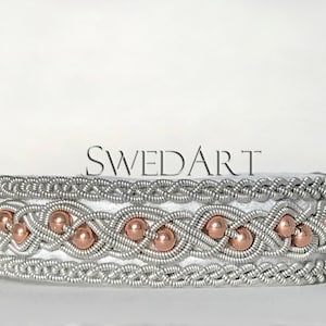 May include: A silver and copper wire bracelet with a braided design and copper beads. The bracelet is on a white background. "SWEDART" is written in the background.