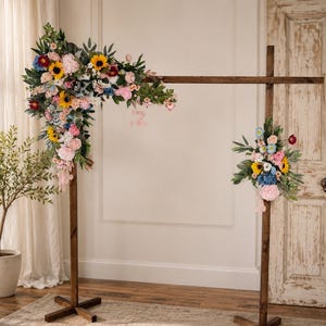 May include: A wooden wedding arch adorned with vibrant flowers, including sunflowers and roses. The arch is stained dark brown and rests on a neutral rug. The flowers are arranged in a cascading style. The arch is approximately 2 meters tall.