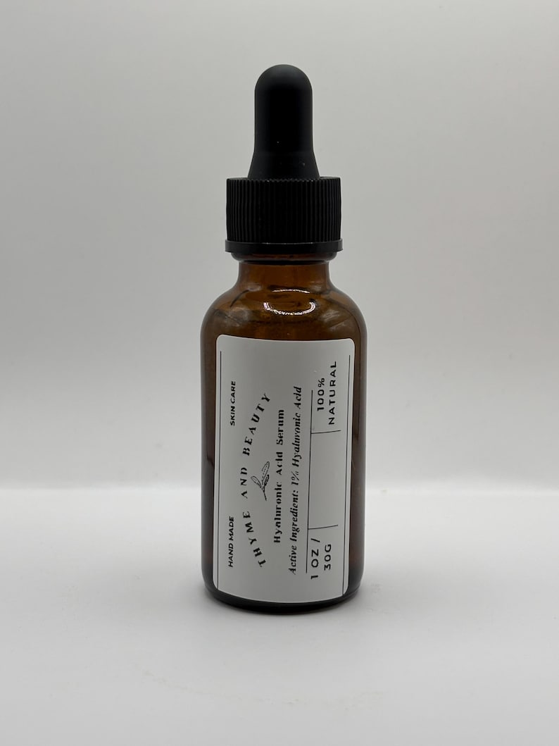 May include: A clear glass bottle with a black dropper top, labeled "THYME AND BEAUTY Hyaluronic Acid Serum". The bottle is 1 ounce and contains 1% hyaluronic acid. It is 100% natural and hand-made.