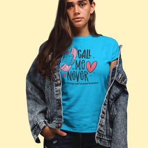 Puede incluir: Una mujer con una camiseta azul con un gráfico de teléfono rosa y el texto "Call Me Never. I'm sassy and sacred woman." También lleva una chaqueta vaquera y pantalones vaqueros azules.