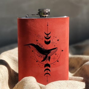 May include: A red leather flask with a silver top and a black whale and moon design.