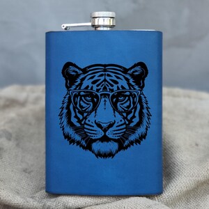 Puede incluir: Una petaca de acero inoxidable azul con una imagen en blanco y negro de un tigre con gafas.