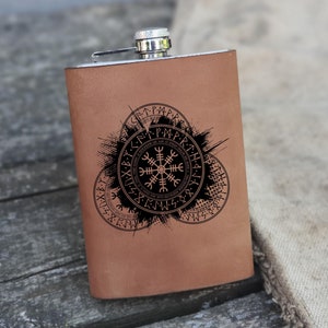 May include: A brown leather flask with a silver top and a black design of a compass with runes around it.