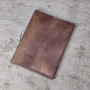 May include: A brown leather passport holder with visible stitching around the edges. The leather has a natural, slightly distressed appearance. The item is rectangular and appears to be handmade.