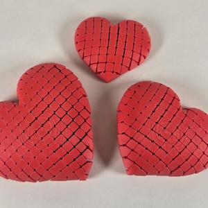 May include: Three red heart-shaped ornaments made of small squares. The hearts are different sizes and are arranged in a triangular shape.