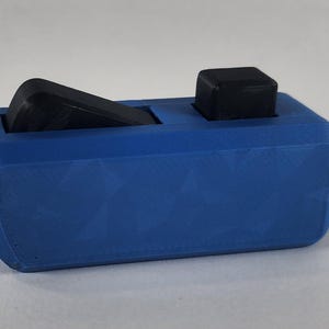 May include: A blue 3D-printed object with two black components. The blue base has a geometric pattern. One black component is rectangular and angled, while the other is a small square. The object is likely a holder or organizer.