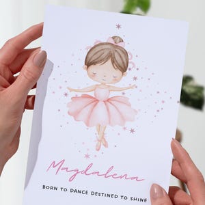 Può includere: Un biglietto di auguri con un'illustrazione ad acquerello di una ballerina con tutù rosa e scarpette da ballo. Il biglietto riporta il nome "Magdalena" in corsivo, con il testo "Born to dance destined to shine" sotto. Stelle rosa sono sparse intorno alla ballerina.