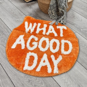 Peut inclure: Tapis rond orange avec le texte "What a good day" en lettres blanches et moelleuses.