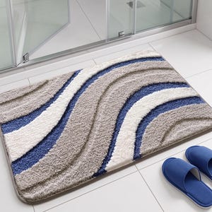 May include: A rectangular bath mat featuring a textured, shaggy pile with a wavy, striped pattern in shades of blue, white, and light grey. The mat has rounded corners and a finished edge, accompanied by a pair of solid blue open-toe slippers.