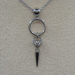 May include: A silver chain necklace with a large silver ring pendant and a smaller silver pendant shaped like a spike.