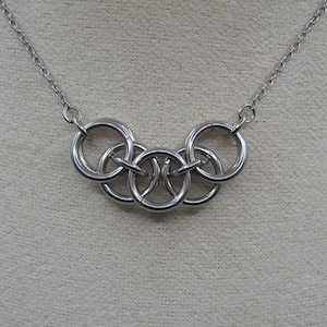 May include: A silver necklace with a five-ring pendant. The rings are interlocked and form a circle.