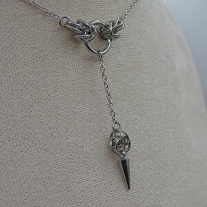 May include: A silver chain necklace with a circular pendant and a pointed, teardrop-shaped charm.