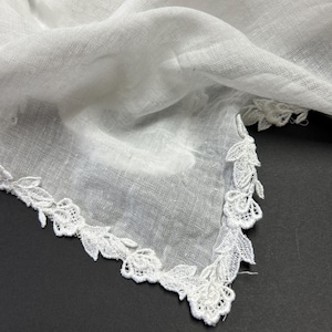 May include: A white, delicate handkerchief with a lace floral border. The fabric appears to be a lightweight linen or cotton, with a slightly sheer quality. The lace trim adds a touch of elegance to this classic accessory.