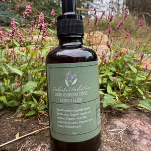 以下が含まれることがあります： 黒いドロッパーキャップが付いた茶色のガラス瓶で、「Salvere Holistics REISHI MUSHROOM TRIPLE EXTRACT ELIXIR」とラベルされています。緑色のラベルには白い文字とラベンダーのイラストがあります。ボトルには59 mlの液体が入っています。背景にはピンクの花があります。