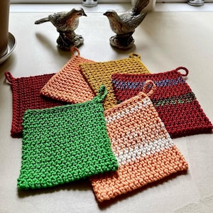 May include: Six crocheted pot holders in various colors, including green, orange, red, and yellow. The pot holders are arranged on a white surface.