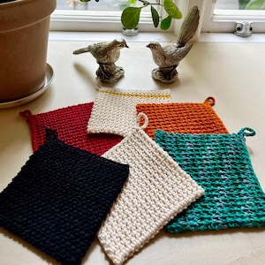 Può includere: Un set di sei presine da forno in maglia di diversi colori, tra cui nero, bianco, arancione e verde. Le presine sono realizzate con un filato testurizzato e sono perfette per proteggere le mani dalle superfici calde.