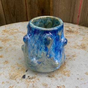 Könnte beinhalten: Eine blaue und grüne Keramikvase mit einer strukturierten, unebenen Oberfläche. Die Vase hat eine breite Öffnung und einen abgerundeten Boden.