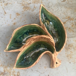 May include: A ceramic dish shaped like three leaves, with a green glaze and brown accents. The dish has three separate compartments.