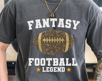 Può includere: Una t-shirt grigio antracite a maniche corte con una grafica di un pallone da football americano marrone dall'aspetto vissuto al centro. Il testo FANTASY FOOTBALL LEGEND è in stampatello bianco, con due piccole stelle gialle ai lati di LEGEND.