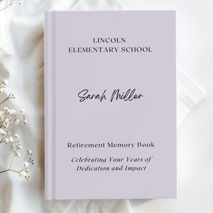 May include: A light purple hardback memory book featuring black text which reads Lincoln Elementary School, Sarah Miller, Retirement Memory Book, and Celebrating Your Years of Dedication and Impact. The book has a clean, professional design.