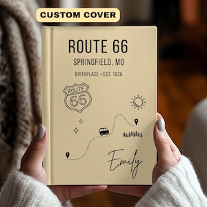 Puede incluir: Un diario beige de la Ruta 66 con texto e ilustraciones en negro. La portada dice "ROUTE 66 SPRINGFIELD, MO BIRTHPLACE • EST. 1926" con un escudo de la Ruta 66, un mapa y el nombre "Emily". El banner superior dice "CUSTOM COVER".