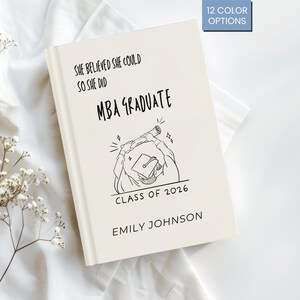Puede incluir: Un diario de graduación de MBA de color crema con el texto "SHE BELIEVED SHE COULD SO SHE DID MBA GRADUATE CLASS OF 2026 EMILY JOHNSON". La portada presenta un dibujo lineal de un graduado. El diario tiene forma rectangular.
