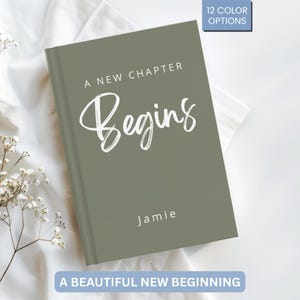 Könnte beinhalten: Ein salbeigrünes Notizbuch mit den Worten "A New Chapter Begins" in weißer Schrift. Der Name "Jamie" ist darunter gedruckt. Oben rechts befindet sich eine blaue Box mit "12 COLOR OPTIONS". Unten steht "A BEAUTIFUL NEW BEGINNING".
