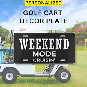 Puede incluir: Placa decorativa negra para carrito de golf con las palabras "WEEKEND MODE CRUISIN'" en blanco. La placa está montada en un carrito de golf blanco en un campo de golf. Las palabras "PERSONALIZADO" y "PLACA DECORATIVA PARA CARRITO DE GOLF" están arriba.