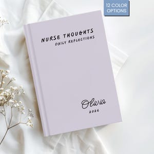 Könnte beinhalten: Ein helllila Notizbuch mit dem Text "NURSE THOUGHTS DAILY REFLECTIONS" in Schwarz. Der Name "Olivia" und das Jahr "2026" sind in schwarzer Schrift gedruckt. Das Notizbuch liegt auf einer weißen Stoffoberfläche.