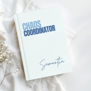 Puede incluir: Un diario de tapa dura color azul claro con el texto "CHAOS COORDINATOR" en letras azules en negrita en la parte superior y el nombre "Samantha" en una fuente cursiva azul oscuro hacia la esquina inferior derecha de la portada.