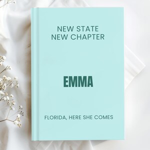 Könnte beinhalten: Ein hellblaues Hardcover-Buch mit dunkelblau-grünem Text, der NEW STATE NEW CHAPTER, EMMA und FLORIDA, HERE SHE COMES lautet. Das Buch hat eine glatte, matte Oberfläche und ist vertikal ausgerichtet, wobei die Vorderseite mit Text zu sehen ist.