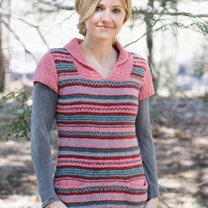 May include: A woman wearing a pink and grey striped knitted sweater with a v-neck and short sleeves. The sweater has a hood and pockets. She is wearing blue jeans.