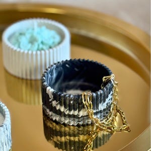 May include: A black and white marbled ceramic trinket dish with a gold chain. The dish has a ribbed design and is sitting on a gold tray.
