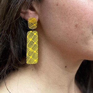 Pode incluir: Brincos geométricos com padrão amarelo com um design preto e amarelo.