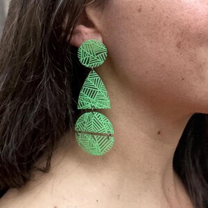 Może przedstawiać: Para zielonych kolczyków z geometrycznym wzorem. Kolczyki składają się z trzech elementów: koła, łzy i drugiego koła. Kolczyki są jasnozielone z czarno-białym wzorem.
