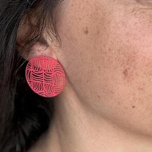 May include: A pair of pink round earrings with a geometric pattern.