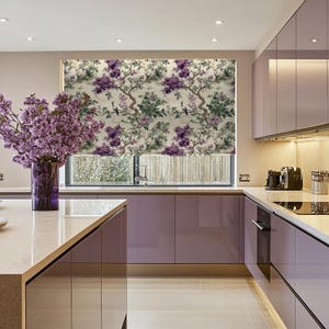 Puede incluir: Una cocina moderna con una ventana que presenta una persiana enrollable estampada con flores moradas y pájaros. Los armarios de la cocina son de color morado claro.