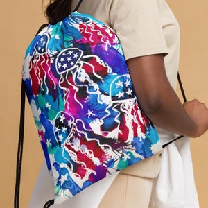 May include: A drawstring backpack with a vibrant, abstract design. The pattern features jellyfish with star-filled caps, set against a backdrop of blue, red, and purple watercolor splashes. Black drawstrings complete the bag.