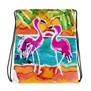 May include: A drawstring bag with a colourful abstract design featuring two pink flamingos standing in a turquoise body of water. The background is a vibrant orange and yellow sunset with green palm trees.