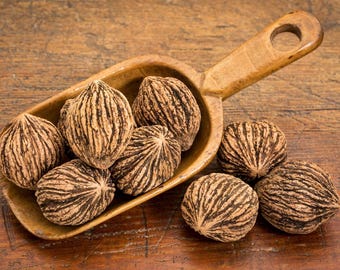 Peut inclure: Une louche en bois remplie de huit noix de noyer brunes et noires. La louche est sur une surface en bois.