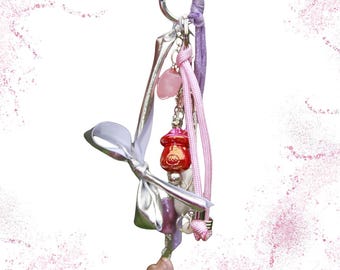 May include: A handmade keychain with a silver-tone metal clip and various charms. Charms include a pink heart-shaped stone, a red and pink decorative element, and a light pink star-shaped charm. The keychain has a white ribbon and the text "finscéal 3/3".