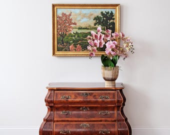 May include: A dark wood antique dresser with three drawers, ornate brass hardware, and curved legs. A framed landscape painting hangs above the dresser, and a potted orchid sits on top. The room has a neutral color palette.