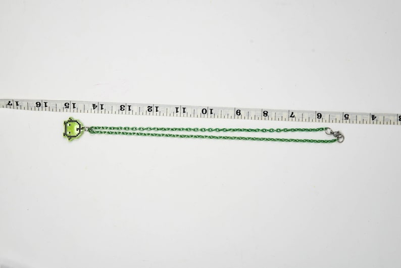 Pu&ograve; includere: Una collana verde con un ciondolo a forma di rana. La catena &egrave; verde e ha una chiusura a moschettone. Il ciondolo &egrave; un design a rana pixelato. La collana misura circa 40 cm di lunghezza.