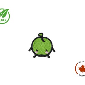 Puede incluir: Parche bordado de manzana verde con una cara sonriente, contornos negros y brazos y piernas peque&ntilde;os. El parche tiene un s&iacute;mbolo vegano y un emblema "Made in Canada".