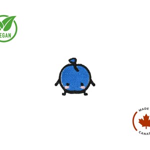 Puede incluir: Parche bordado con un simp&aacute;tico personaje de ar&aacute;ndano azul de estilo caricatura, con contornos negros y mejillas rosas. El parche es redondo y tiene brazos y piernas peque&ntilde;os. Tambi&eacute;n se ve un s&iacute;mbolo vegano verde y un logotipo "Made in Canada".