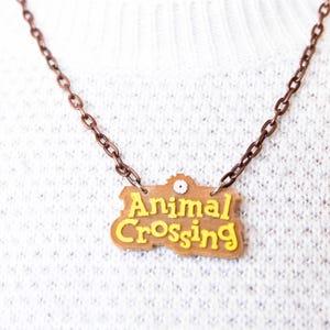 Peut inclure: Un collier en chaîne de cuivre avec un pendentif en plastique brun et jaune qui dit "Animal Crossing".