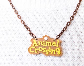 May include: A copper chain necklace with a brown and yellow plastic pendant that says "Animal Crossing".