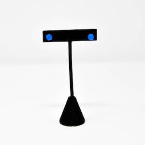 Könnte beinhalten: Ein Paar blaue Ohrstecker, die auf einem schwarzen Ohrringständer ausgestellt sind.