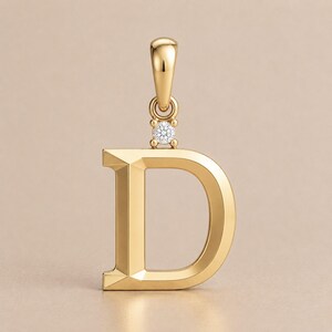 May include: A gold-colored pendant in the shape of the letter "D". The pendant has a small, round diamond accent and a loop at the top for a chain. The pendant is made of a shiny, reflective metal.