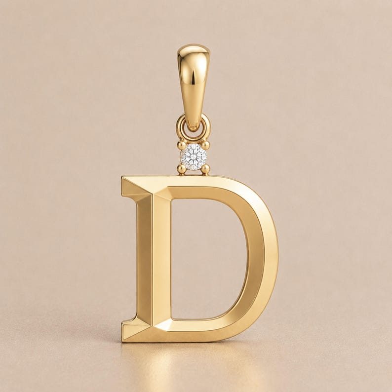 May include: A gold-colored pendant in the shape of the letter "D". The pendant has a small, round diamond accent and a loop at the top for a chain. The pendant is made of a shiny, reflective metal.
